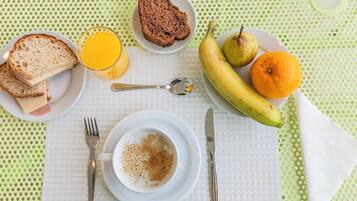 A breakfast setting with bread, fruit, juice, and a cup of coffee on a table.