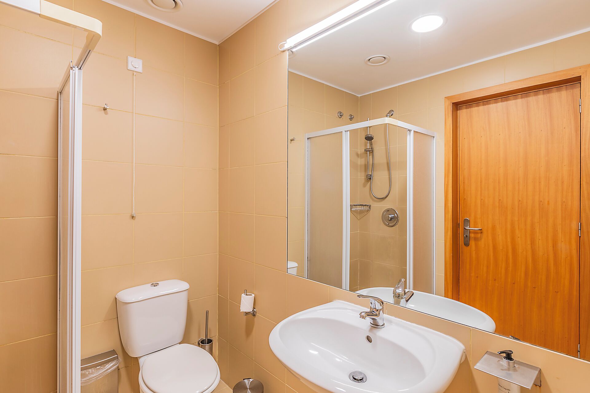 Un baño con inodoro, lavamanos, ducha y puerta de madera.