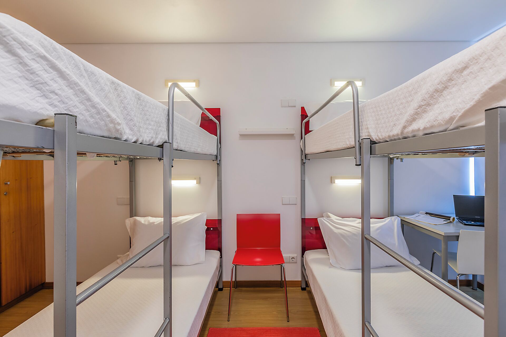 Un dormitorio tipo camarote con dos camas, un escritorio y una silla roja.