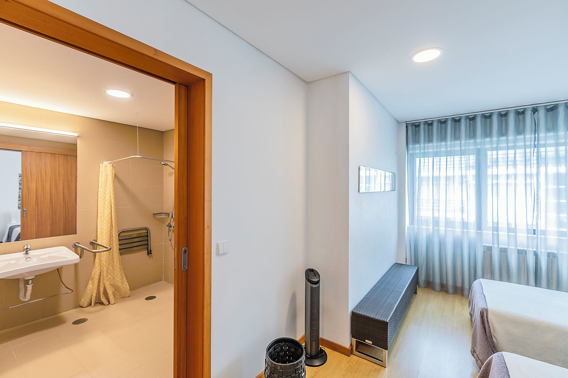 A hotel room with a bathroom, a bed, a heater, and a window with curtains.