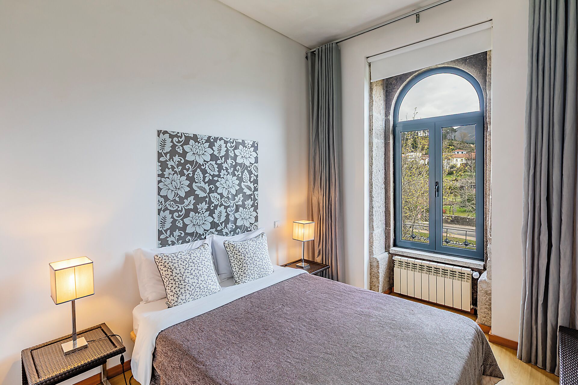Een slaapkamer met een groot bed, twee bedlampen, een raam met gordijnen en een wanddecoratie.