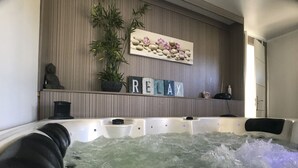 A hot tub with water, surrounded by a wooden wall with a 'RELAX' sign, a statue, and a potted plant. - Les Yourtes à la Ferme des Epis (Ouffieres)