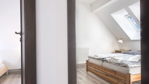 Une chambre avec un plafond en pente, un puits de lumière, un lit en bois, une table de chevet et une commode.