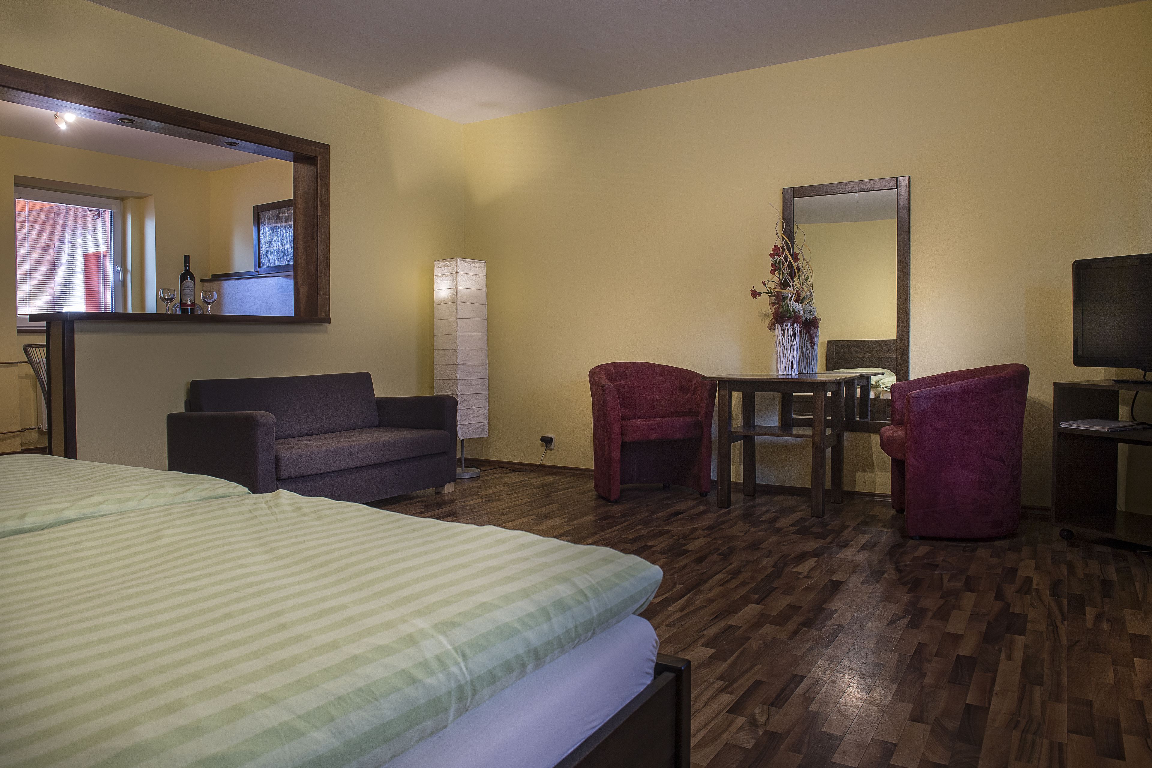 A hotel room with a bed, two armchairs, a small table, a mirror, and a television.