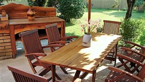 Un ensemble de mobilier de jardin en bois comprenant une table et six chaises, un vase avec des fleurs et un banc en bois à l’arrière-plan.