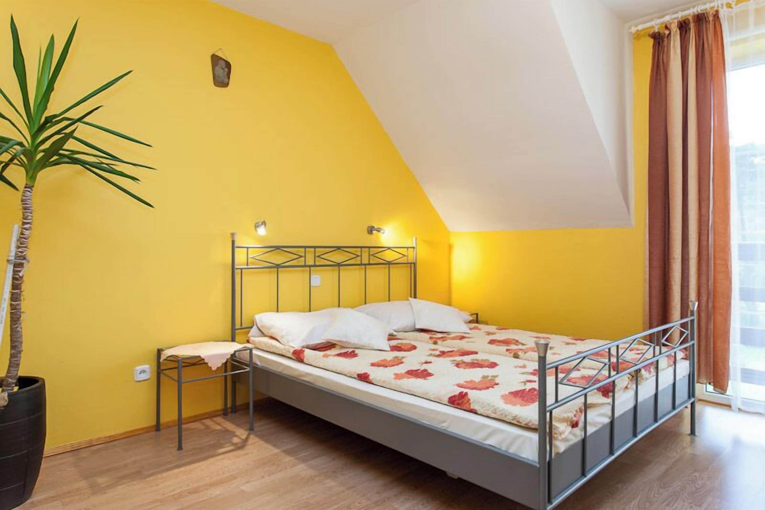 Una cama individual con estructura metálica, una mesita de noche, una planta en maceta y una ventana con cortinas.