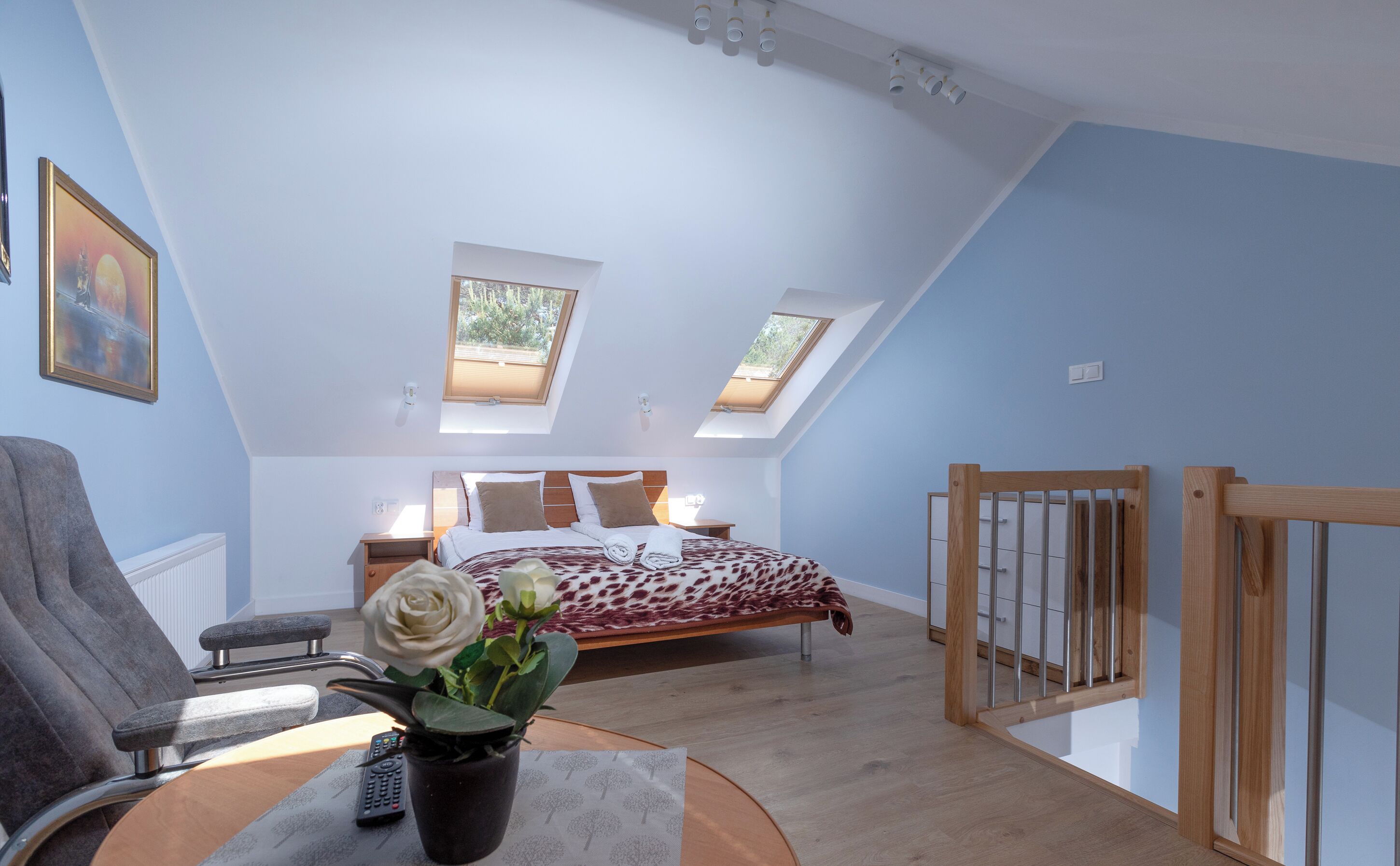 A bedroom with a skylight, a bed with a patterned bedspread, a potted plant, and a chair.