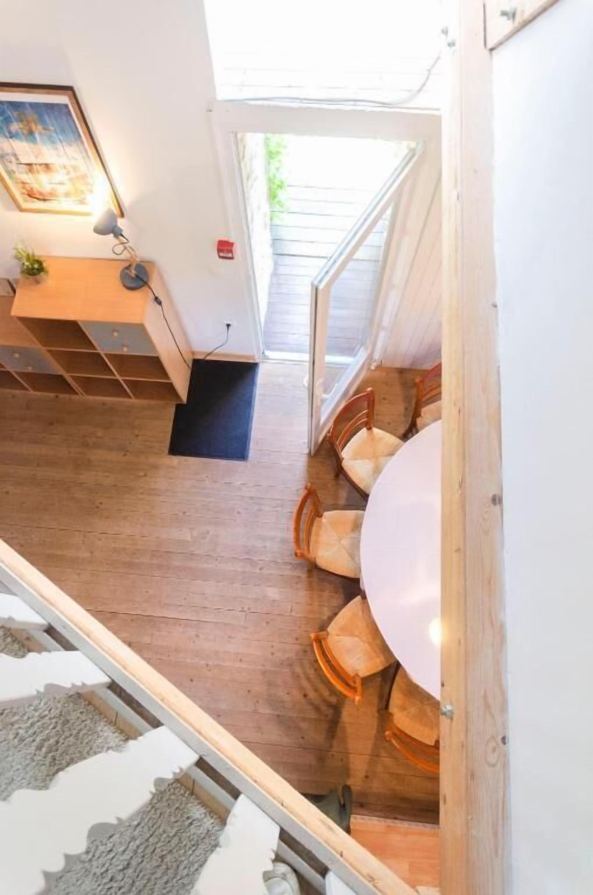 Un interno moderno con pavimento in legno, zona pranzo con sedie e tavolo, e una scala che conduce a un livello superiore.