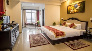 A hotel room with a large bed, a desk with a computer, a chair, a window, and a painting on the wall. - Daizzo Maple Residency (Gangtok)