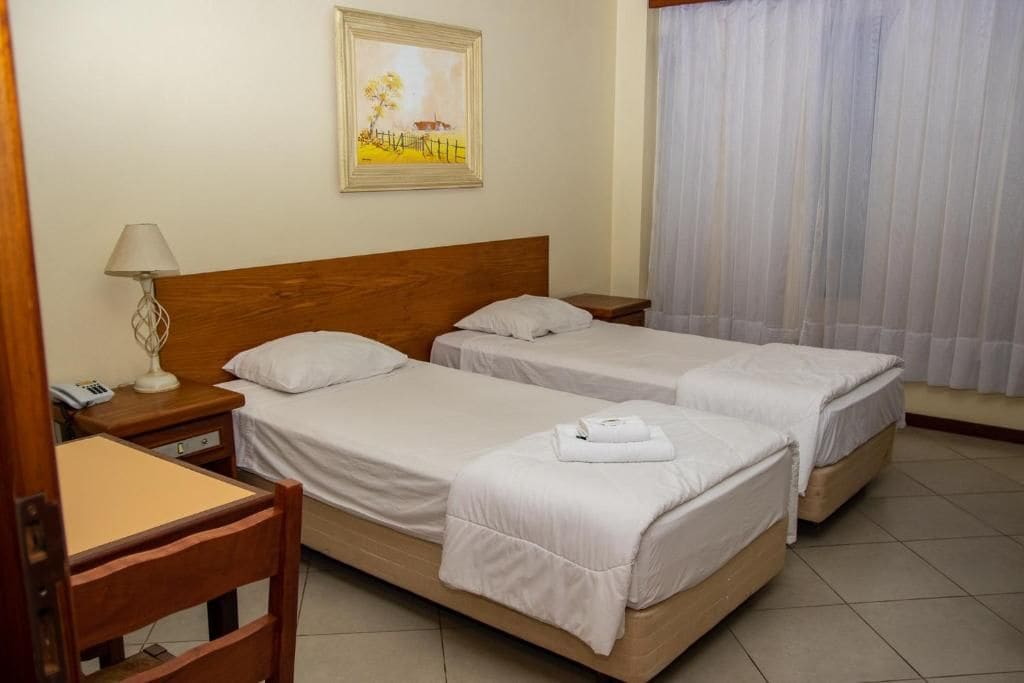 A hotel room with two single beds, a desk with a chair, a lamp, and a painting on the wall.