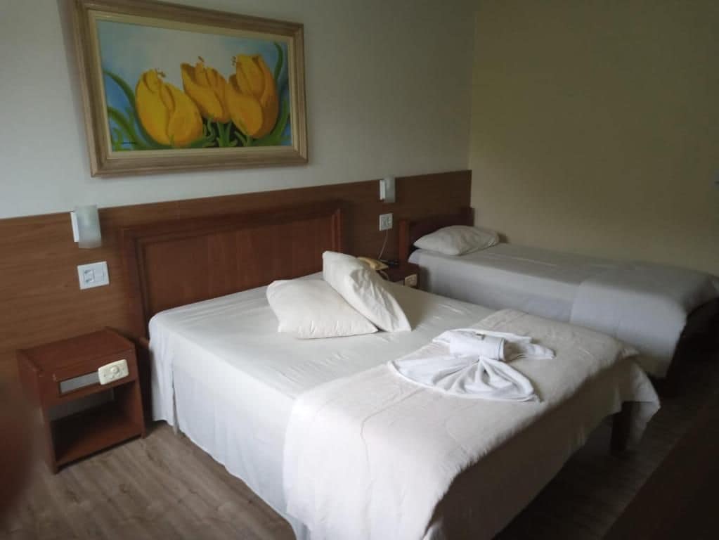 Habitación de hotel con dos camas, un cuadro de flores amarillas en la pared y una mesita de noche con una lámpara.