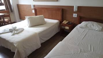A hotel room with two single beds, a wooden headboard, a bedside table with a lamp, and a painting on the wall.