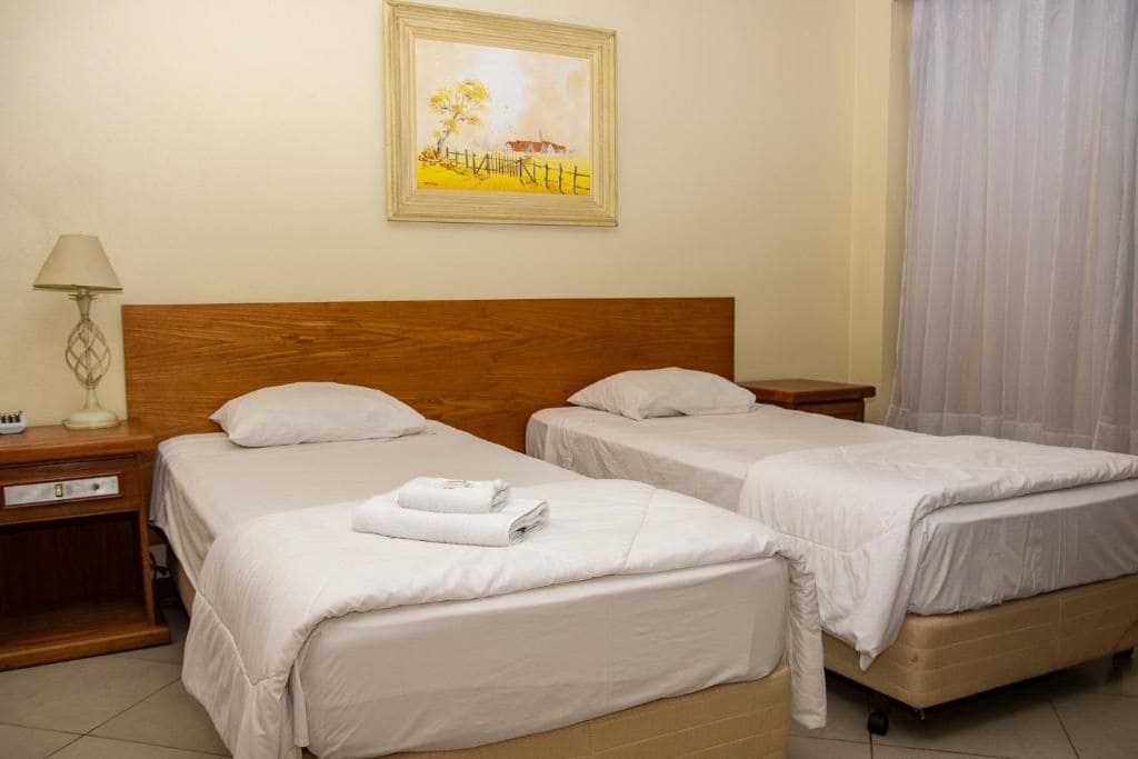 Una habitación de hotel con dos camas individuales, un cabecero de madera, una mesita de noche con una lámpara y un cuadro en la pared.
