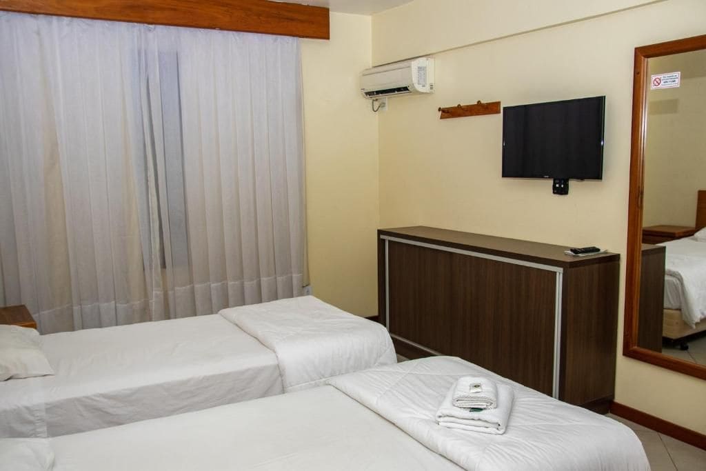 Ein Hotelzimmer mit zwei Betten, einem Fernseher, einer Klimaanlage und einem Spiegel.