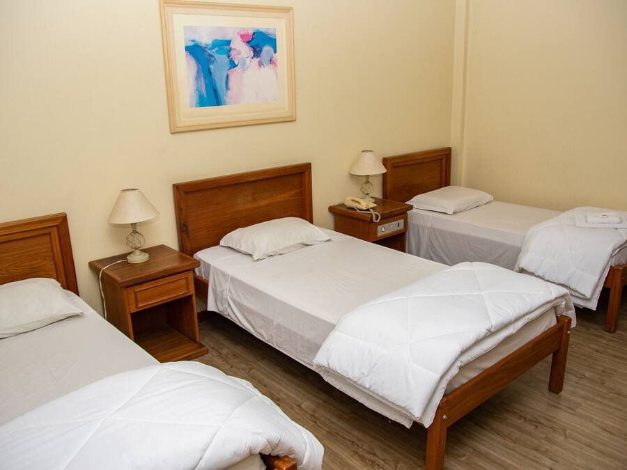 Hotelkamer met vier eenpersoonsbedden, houten hoofdeinden, nachtkastjes met lampen en een lijst met een abstract schilderij aan de muur.