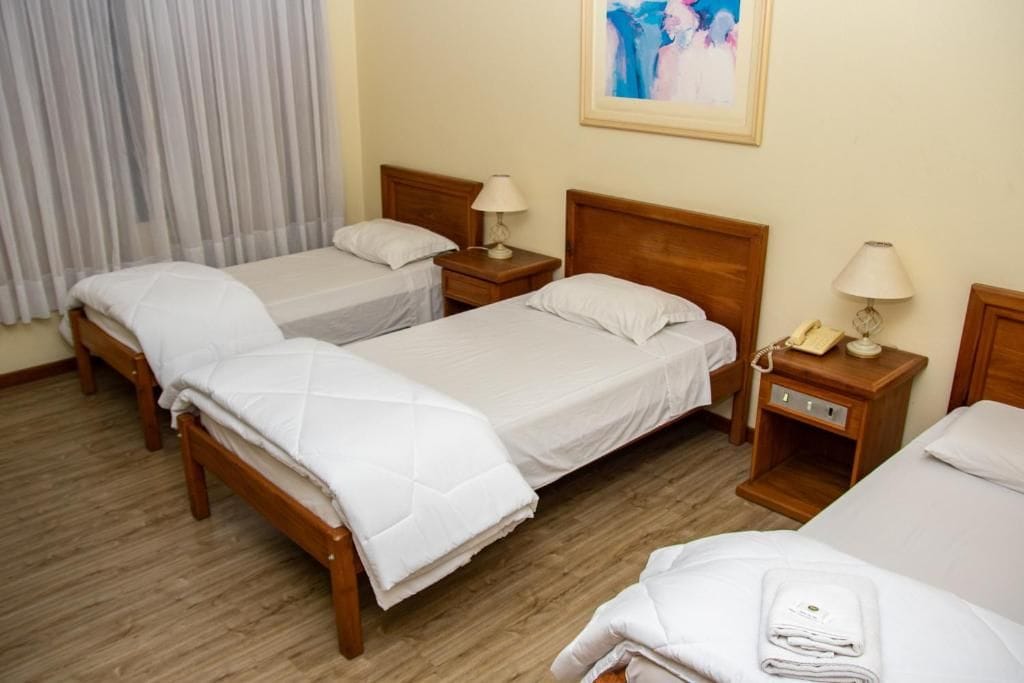 A hotel room with two beds, a wooden headboard, bedside tables with lamps, and a painting on the wall.
