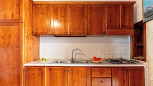Una cocina con armarios de madera, un salpicadero blanco de azulejos, un lavabo de acero inoxidable y una estufa a gas.