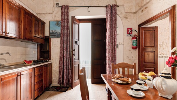 Una cocina con armarios de madera, una estufa y una mesa de comedor con platos, tazas y una tetera.