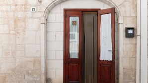 Puerta de madera con el número 19 encima, una pequeña rejilla de ventilación debajo y una caja eléctrica fijada a la pared a la derecha.
