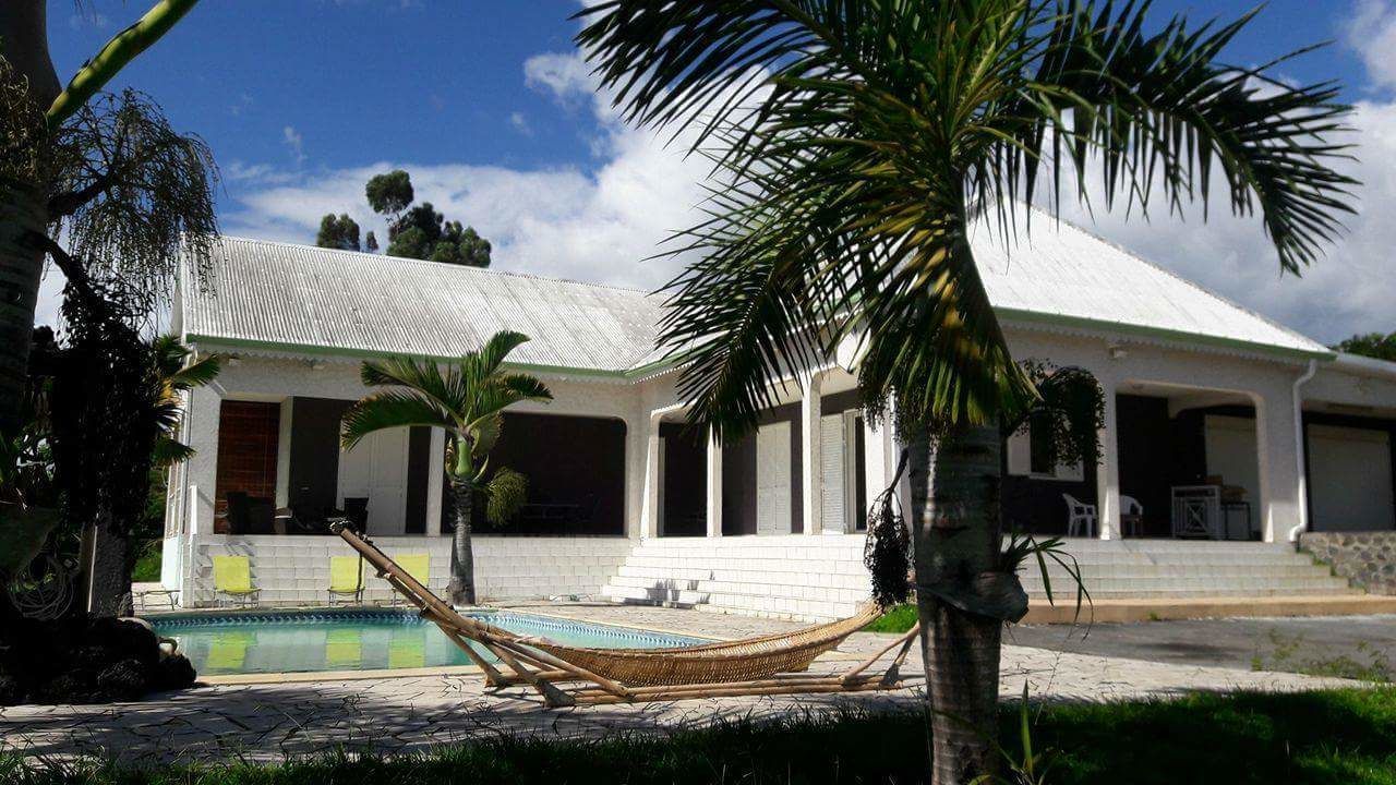 A white building with a swimming pool, palm trees, and a hammock.