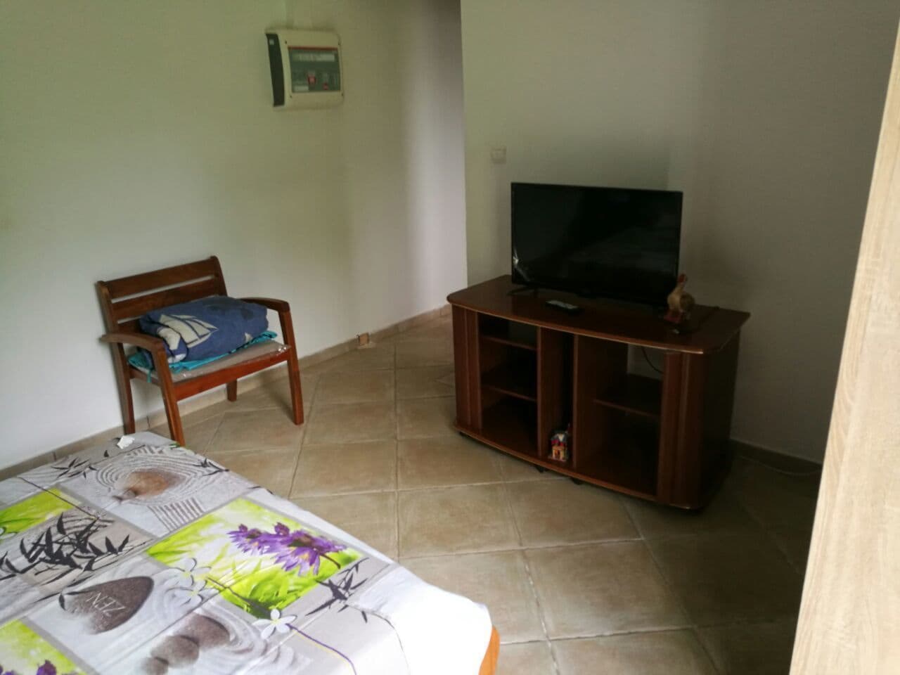 Ein Wohnzimmer mit einem Holzstuhl, einem Fernseher auf einem Holzschrank und einem Fliesenboden.