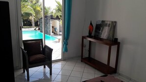 Habitación con vista a una piscina, una silla, una consola con un cuadro y una cortina color turquesa.