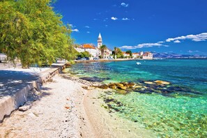 A coastal town with clear waters, a sandy beach, and a prominent church with a tower.
