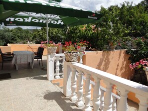 An outdoor patio with a table and chairs, potted plants, and a green umbrella.