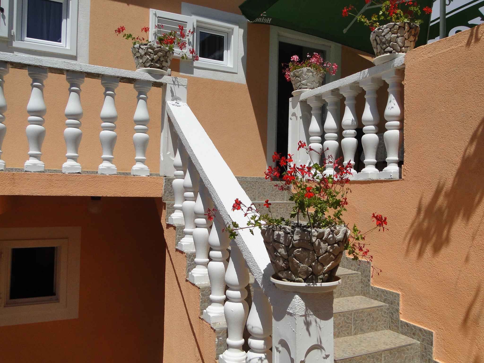 A staircase with white balustrades and stone railings, leading to a balcony with potted plants.