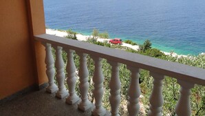 Un balcon avec vue sur la mer et une voiture rouge garée sur la plage.