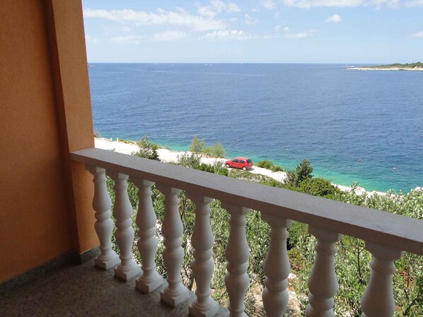 A balcony with a view of the sea and a red car parked on the beach.