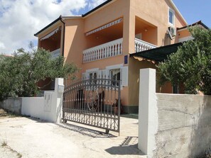 A two-story building with a balcony, a gated entrance, and a concrete wall.