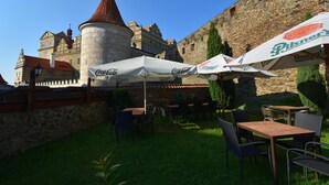 An outdoor seating area with tables and chairs, umbrellas, and a stone building in the background. - Hotel Gurmán (Horšovský Týn)