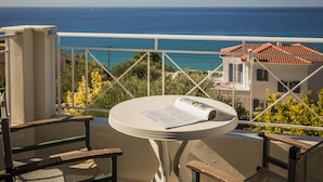 A balcony with a table and chairs, overlooking a coastal view.