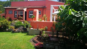 Una casa rossa con tetto in tegole, circondata da un giardino curato e ricco di piante e fiori.