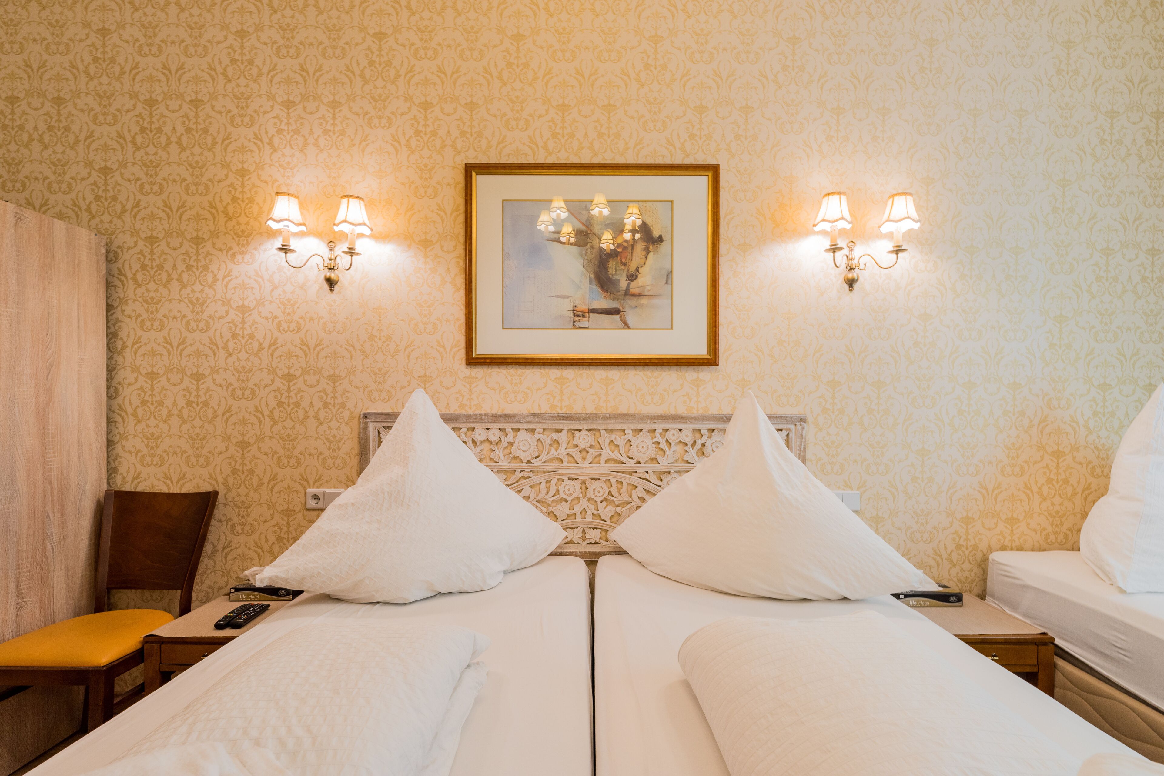 Een hotelkamer met twee bedden, een nachtkastje, een stoel en een ingelijst foto aan de muur.