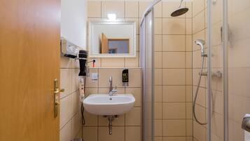 A bathroom with a sink, mirror, shower, and a door.