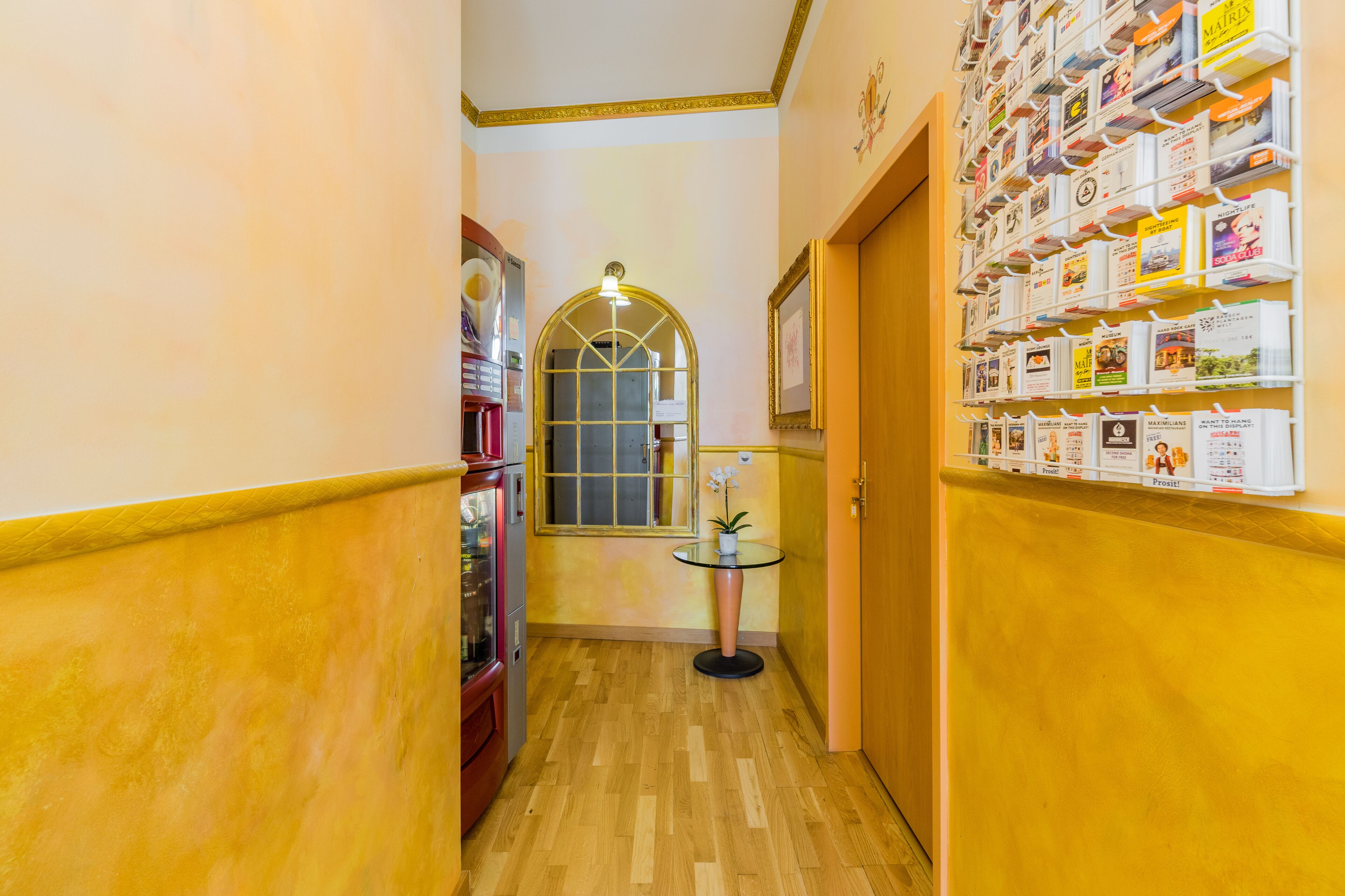A narrow hallway with wooden flooring, a glass table with a potted plant, and a wall with a bookcase.