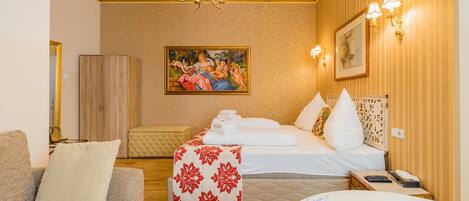 A hotel room with a bed, a sofa, a wooden wardrobe, a painting on the wall, and a chandelier.