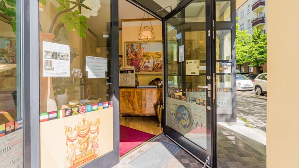 Entrada de un hotel con puerta de vidrio, alfombra roja y un cartel.