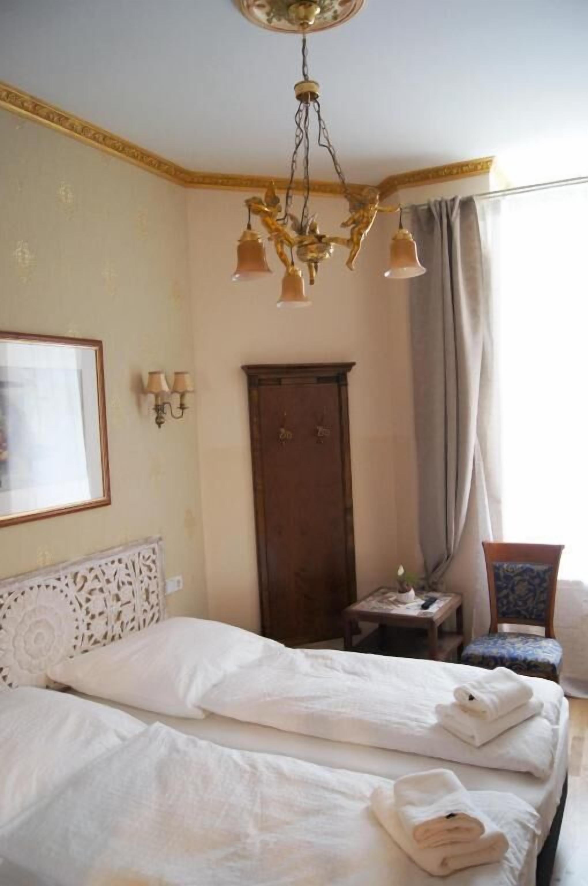 A hotel room with a large bed, a wooden wardrobe, a small table with a lamp, and a chair.