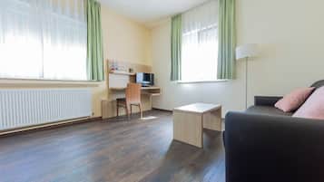 A room with a desk, chair, TV, and a sofa.