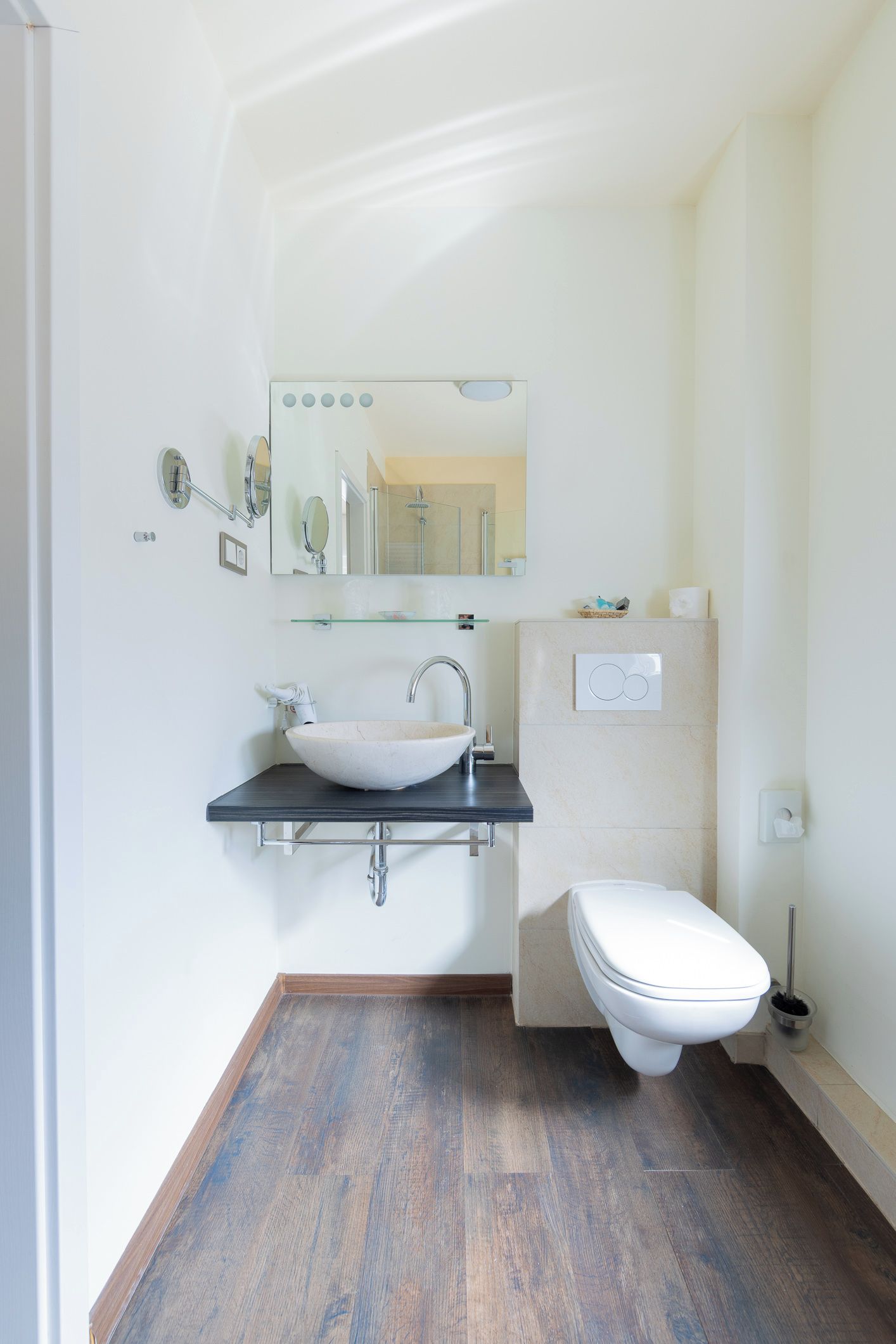 Un bagno moderno con un lavandino bianco, un water e uno scaffale in vetro sopra il lavandino.