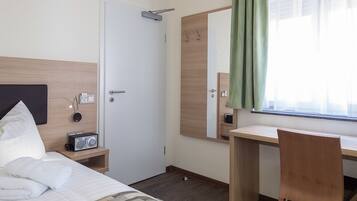 Habitación de hotel con cama, escritorio, silla, espejo, reloj y ventana con cortinas.