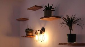A corner of a room with wooden shelves holding potted plants and a wall-mounted light fixture. - Hotel Restaurante Lorca (Weinsberg)