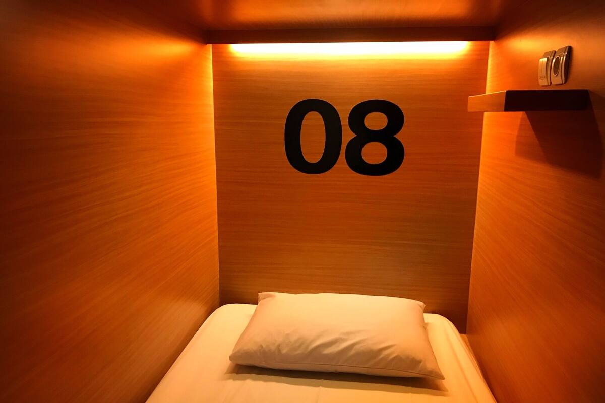 A single bed with a white pillow in a room with wooden walls and a number '08' on the wall.