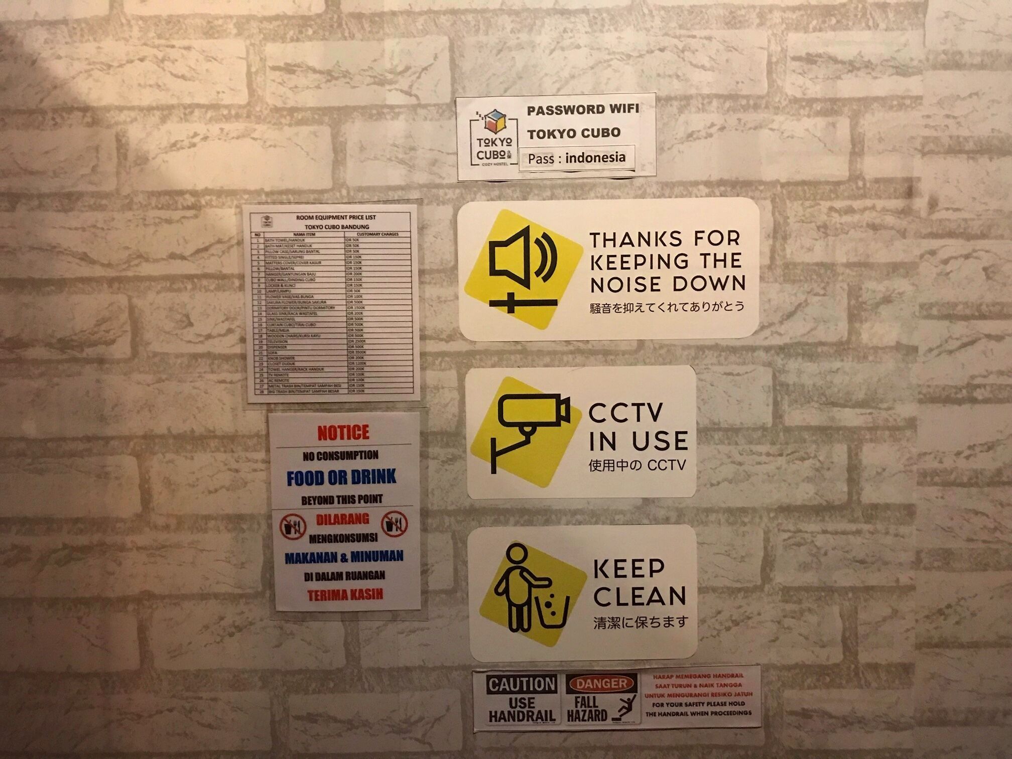 Een muur met diverse borden, waaronder een prijslijst voor kamerfaciliteiten, wifi-toegangscode, geluidsreductie, cameratoezicht, verbod op het nuttigen van eten en drinken, en een bord dat vraagt om netheid te bewaren.