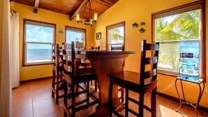 Una cocina con sillas de madera, una barra y grandes ventanas con vistas al océano.