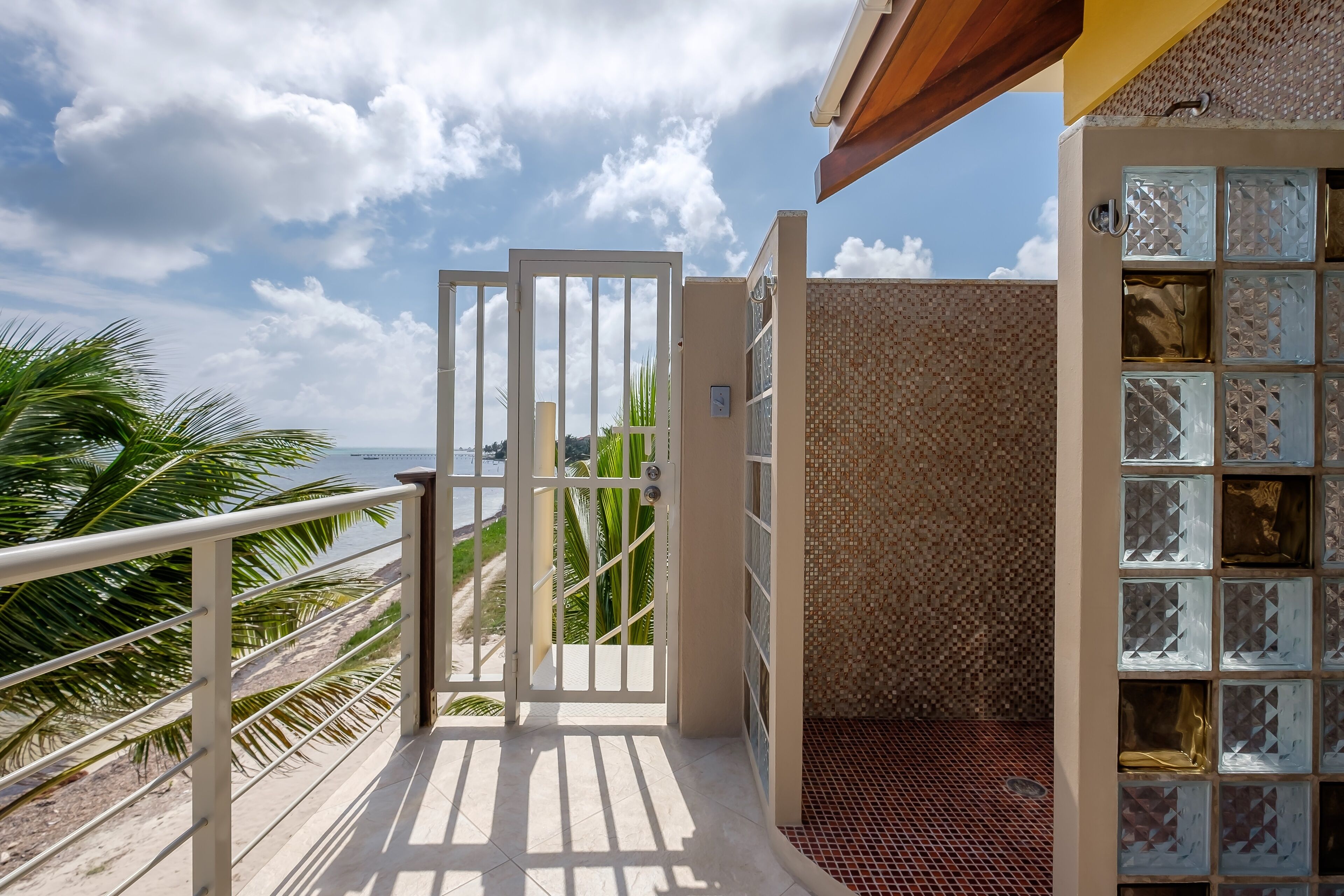 A balcony with a view of the beach, a tiled wall with glass panels, and a metal railing.