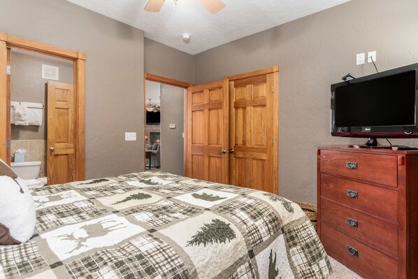 A bedroom with a quilted bedspread, wooden wardrobe, and a television on a stand.